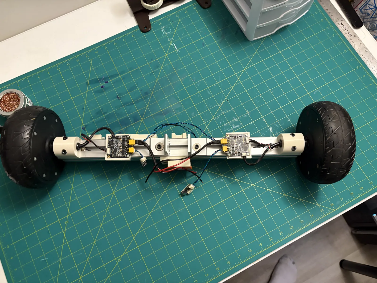 Top-down view of the robot base on a green cutting mat, showing both hub motors, both Moteus controller boards, XT30 connectors, and the twisted-pair CAN bus running between them.