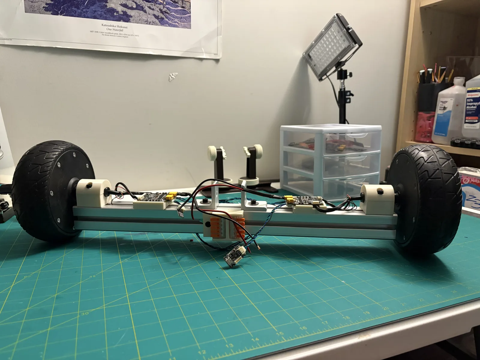 The robot base on a cutting mat: a length of aluminium extrusion with a hub motor at each end, printed axle mounts, two controller boards, and orange lever connectors.