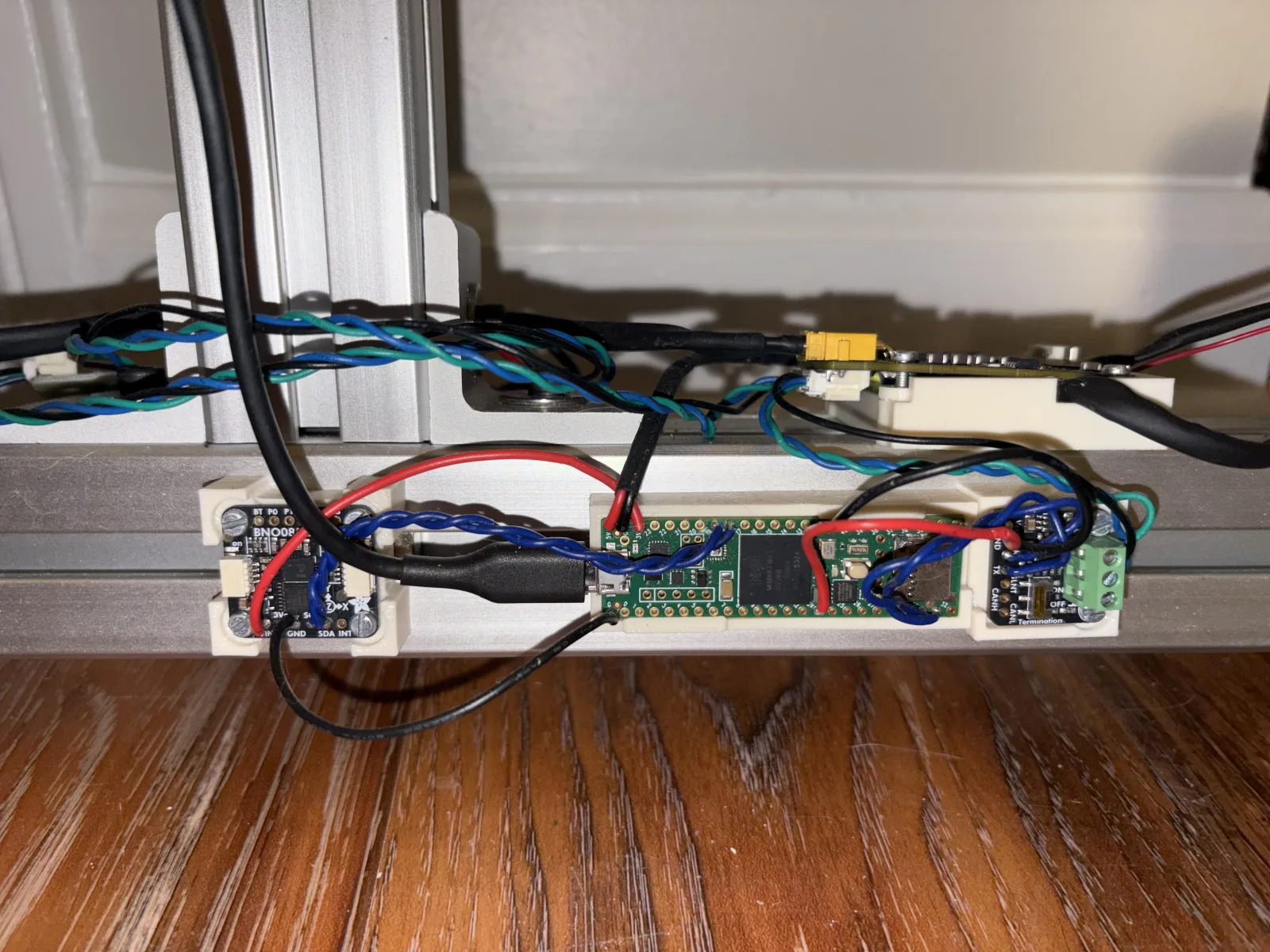 Close-up of the BNO085 IMU, Teensy 4.1, and CAN transceiver mounted in printed brackets clipped to the aluminium base rail of the robot.